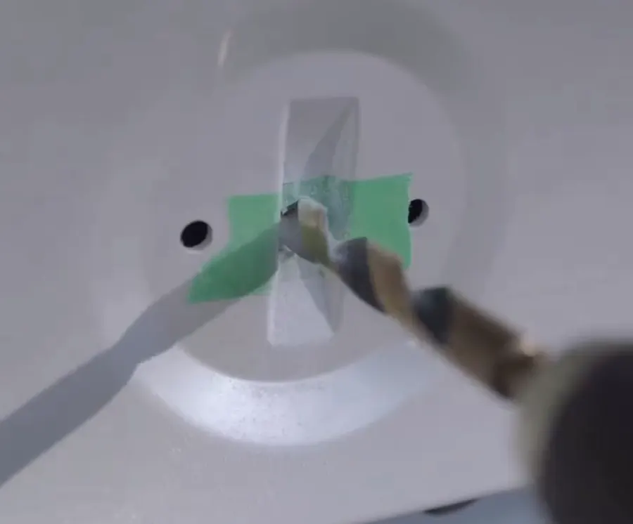 A drill bit going through masking tape into a car boot lid to fit an alternative badge