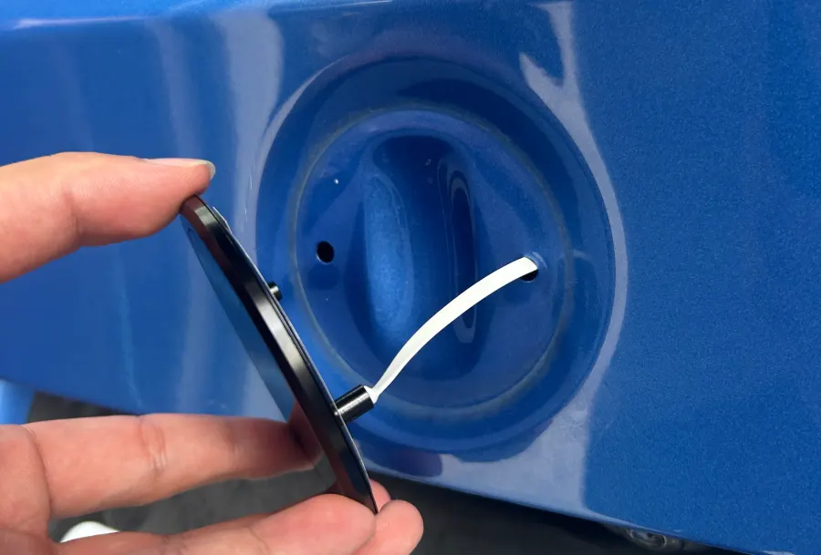 A hand pressing the emblem into the factory recess, its lead passing through an existing hole